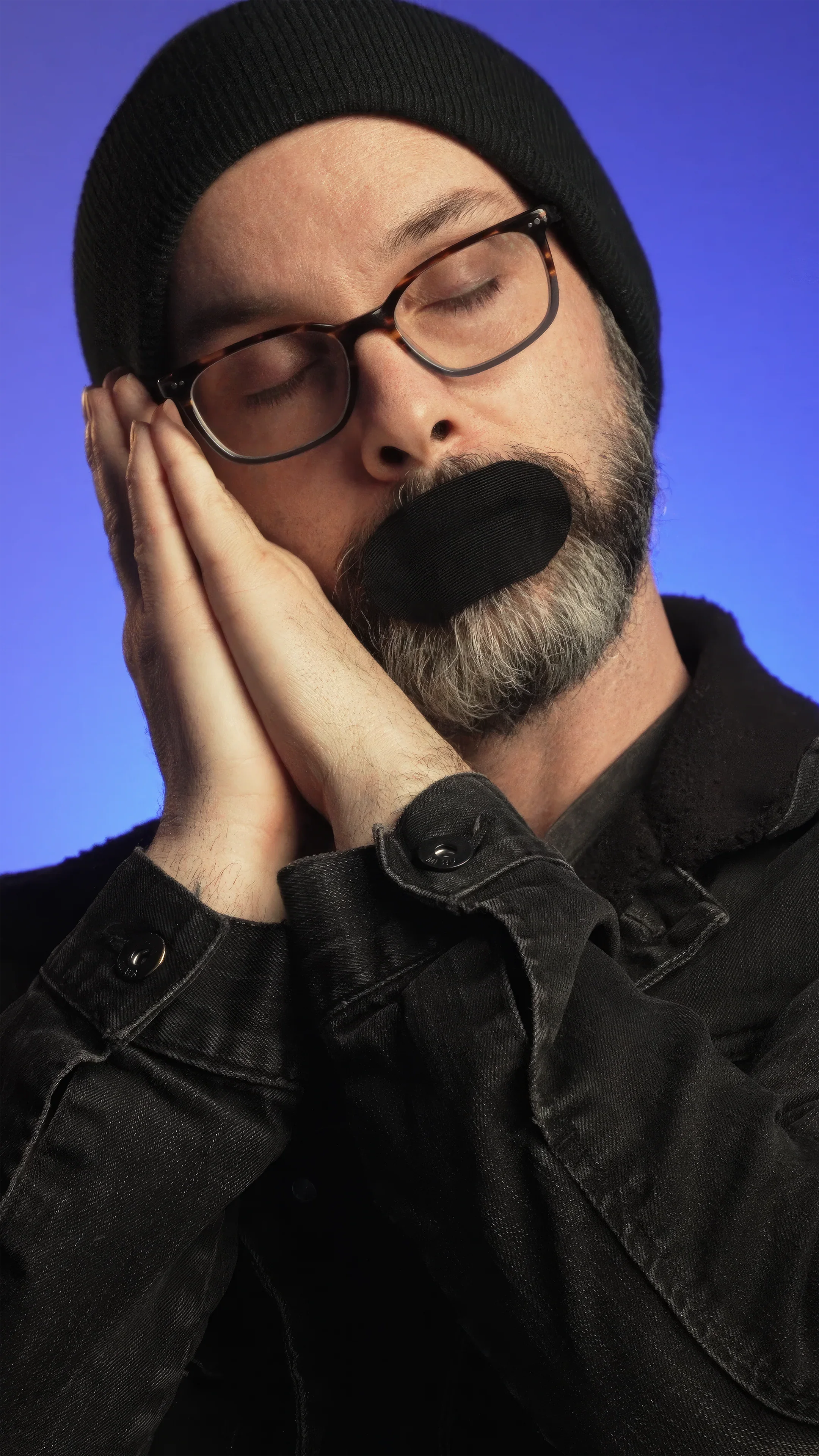 Bearded man wearing Hostage Mouth Tape, simulating sleep with hands near face