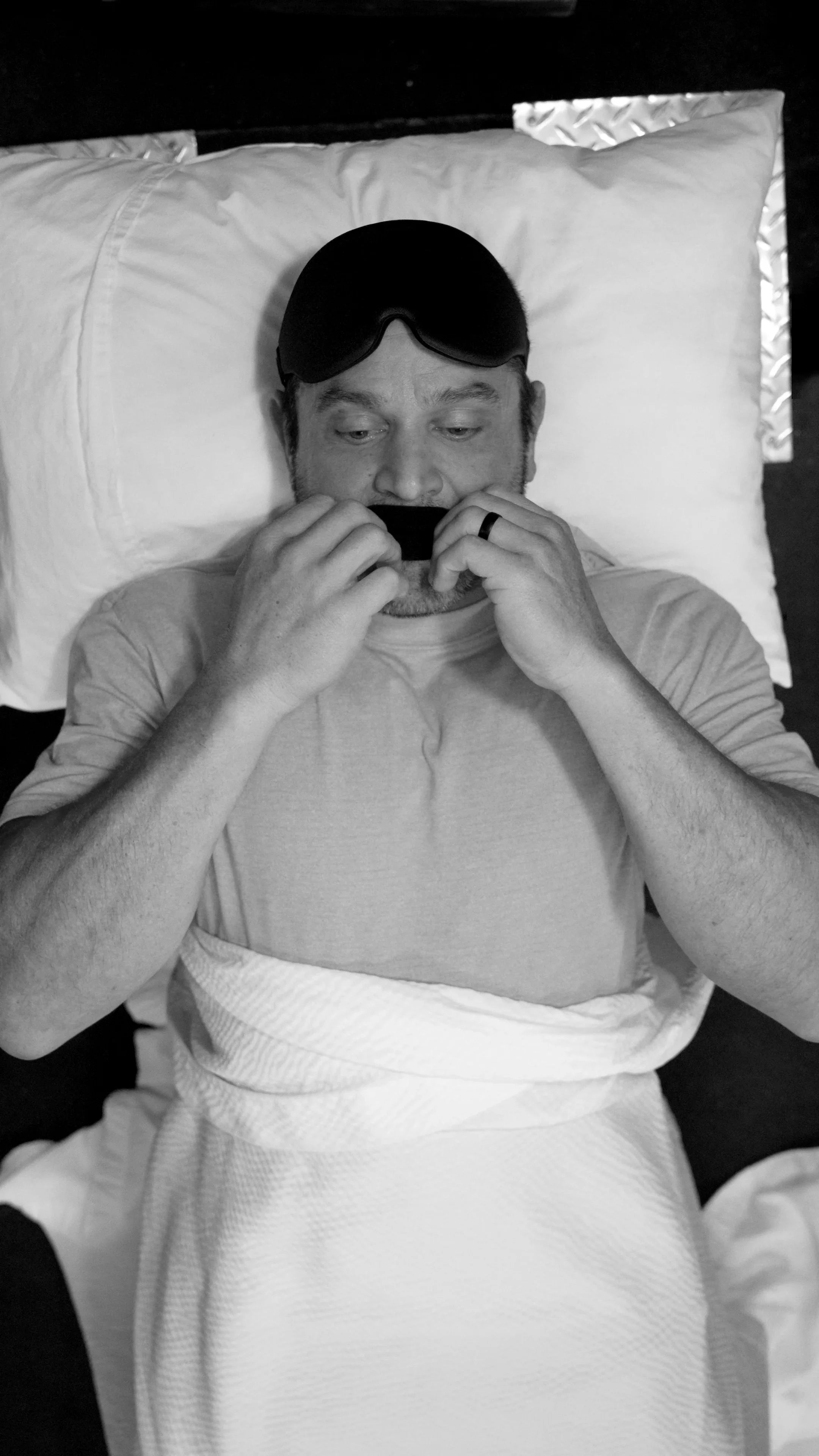 Man in bed applying Hostage Tape mouth tape before sleep for better breathing.
