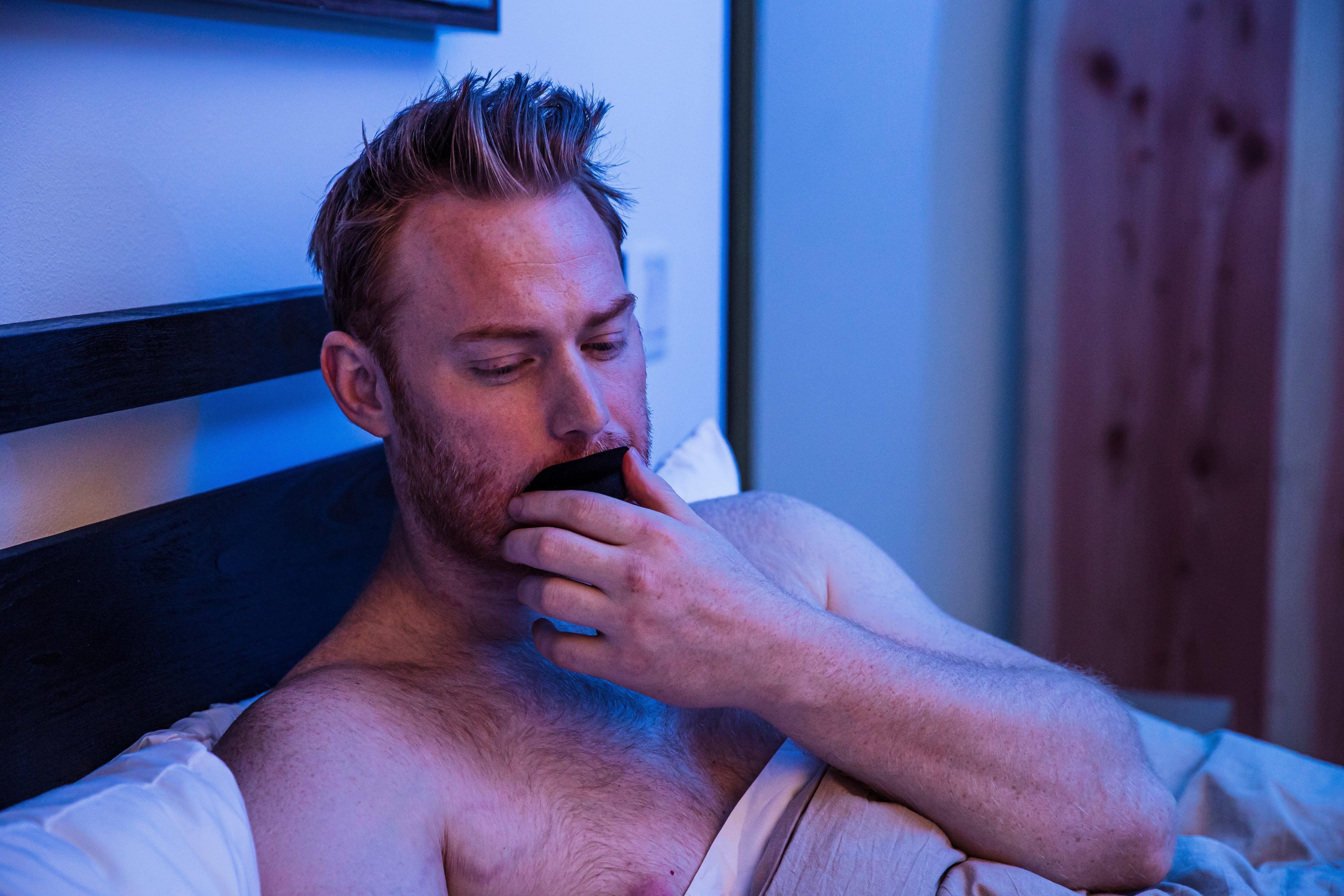 Man lying in bed wearing Hostage Mouth Tape for quieter, restorative sleep and nasal breathing.