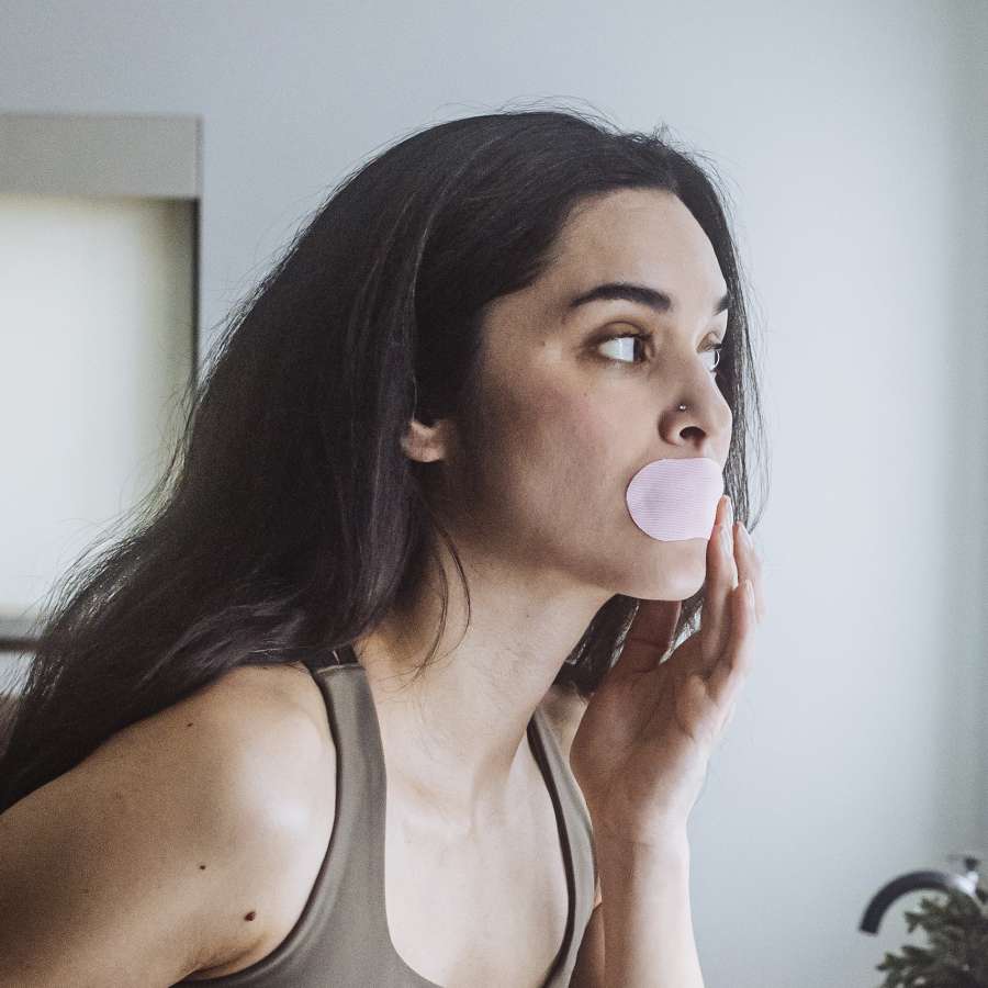 Woman applying pink Hostage Tape mouth strip – breathable and comfortable
