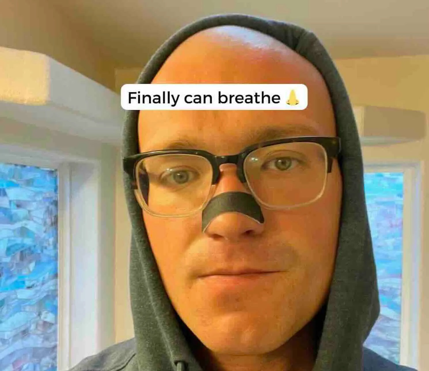 Person wearing a green hood with text overlay 'Finally can breathe' in a room with windows.