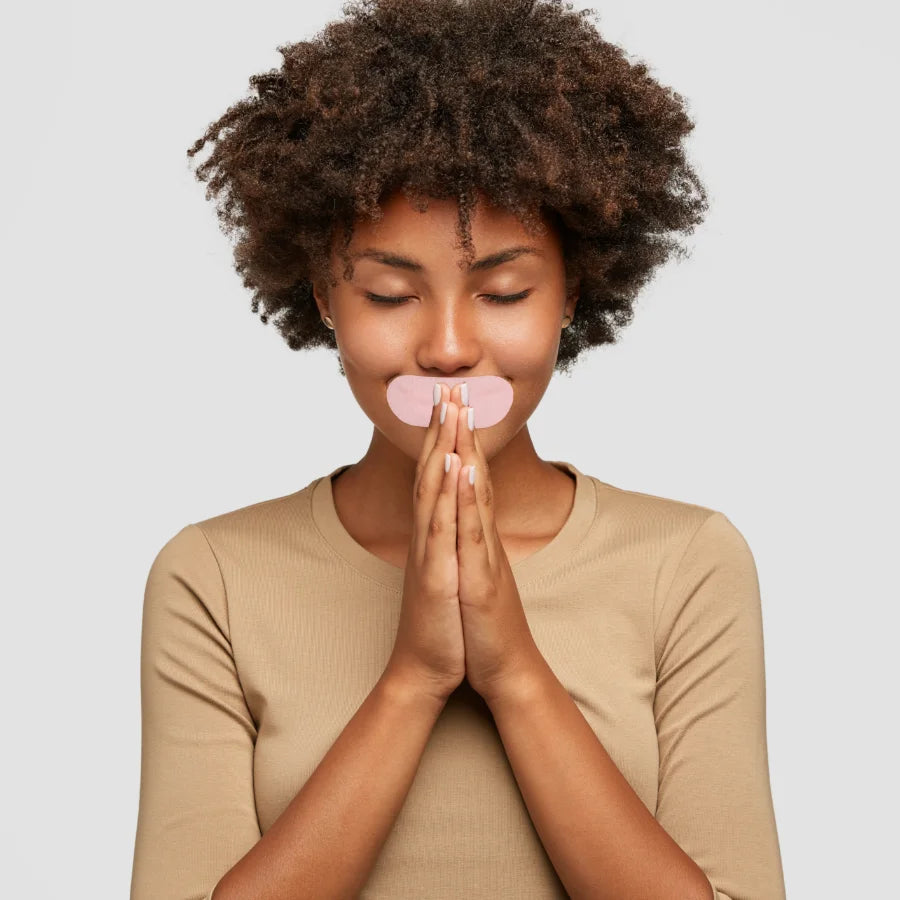 Smiling woman wearing pink Hostage Mouth Tape in prayer pose for better sleep and breathing