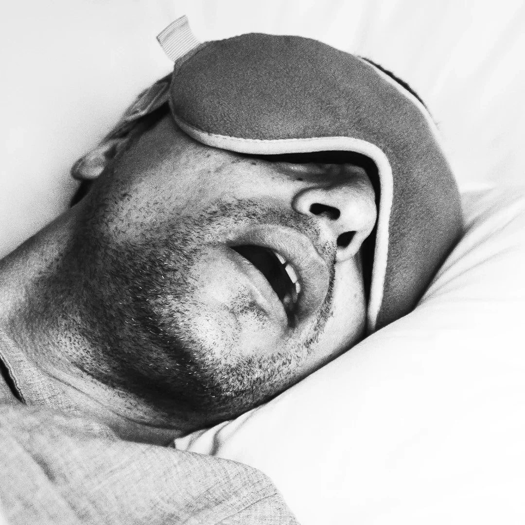Male sleeper with open mouth and sleep mask in bed