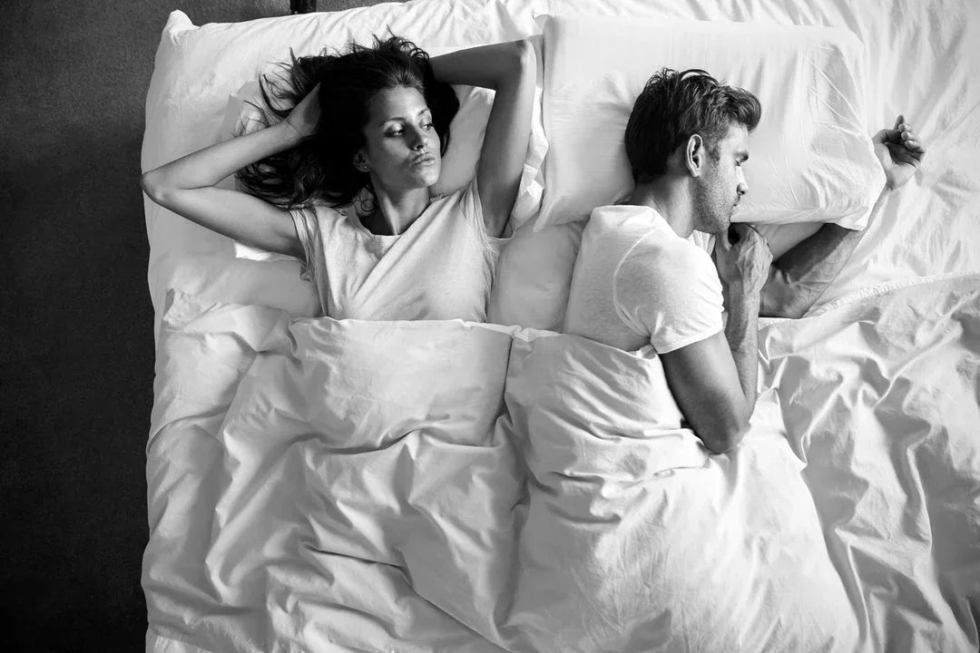 Frustrated woman in bed beside snoring man